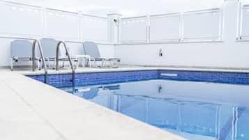 A swimming pool with a tiled edge, metal handrails, and two lounge chairs.