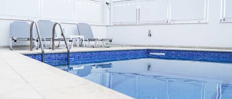 A swimming pool with a tiled edge, metal handrails, and two lounge chairs.