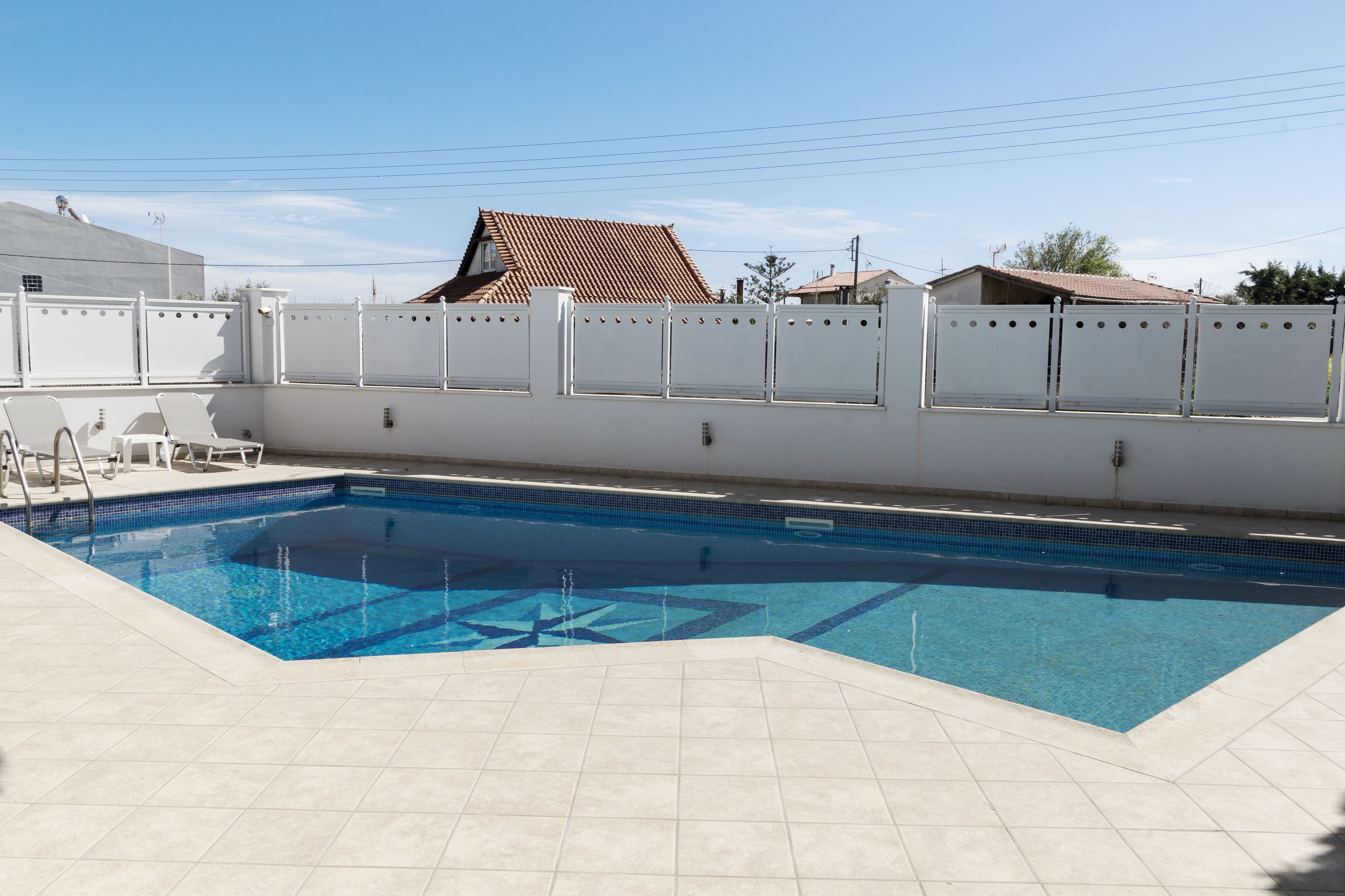 Una piscina amb una terrassa enrajolada, una tanca blanca i un cel blau i clar.