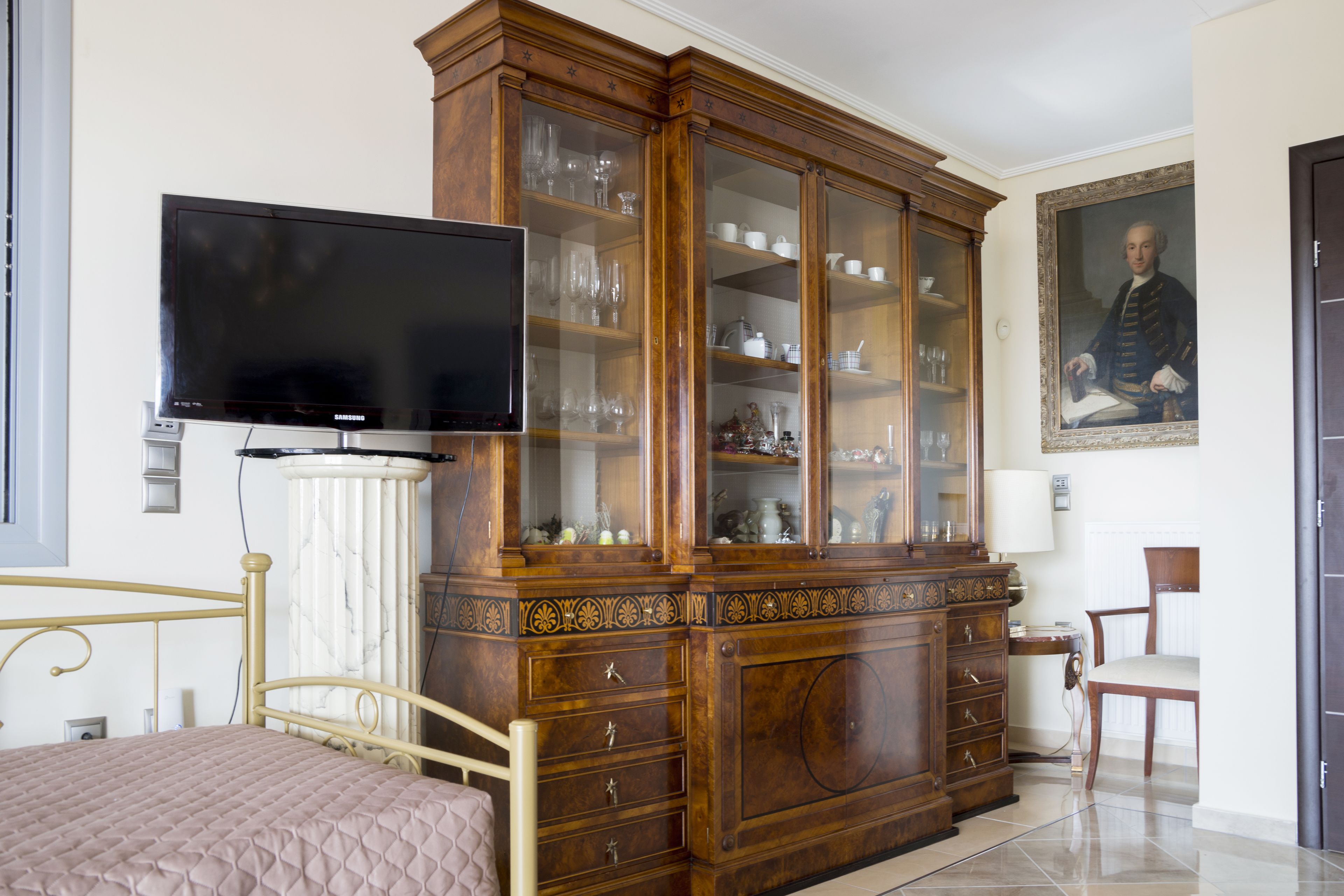 A bedroom with a bed, a television, a wooden cabinet with glass doors, and a chair.