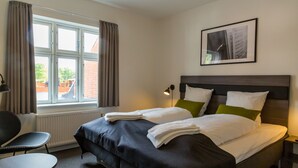 Habitación de hotel con cama, una silla, una mesa y ventana con cortinas.