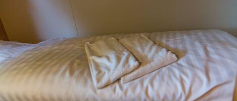 A bed with white linens and a folded beige towel.