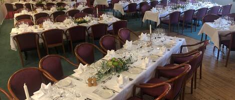 A banquet hall with long tables set for dining, surrounded by chairs.