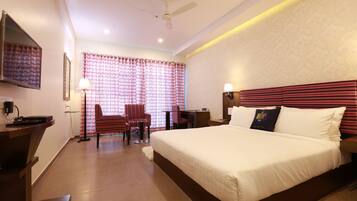 A hotel room with a large bed, a desk with a chair, a television, and a ceiling fan.