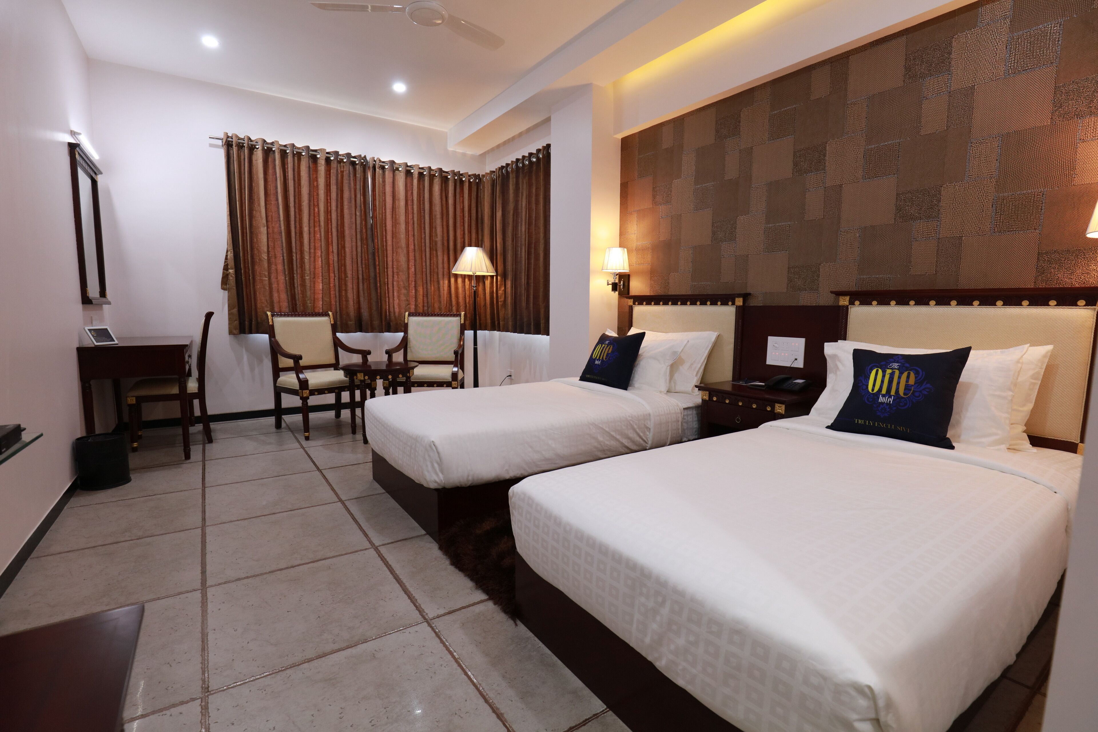 A hotel room with two beds, a desk, a chair, and a lamp.