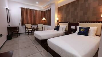 A hotel room with two beds, a desk, a chair, and a lamp.