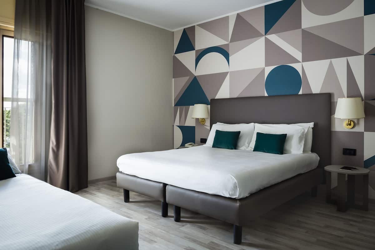 A modern hotel room with a large bed, bedside lamps, a small bedside table, and a geometric-patterned wall.