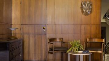 A modern interior with a wooden panel wall, a dark wooden cabinet, two wooden chairs, a small table with a plant, and a staircase in the background.
