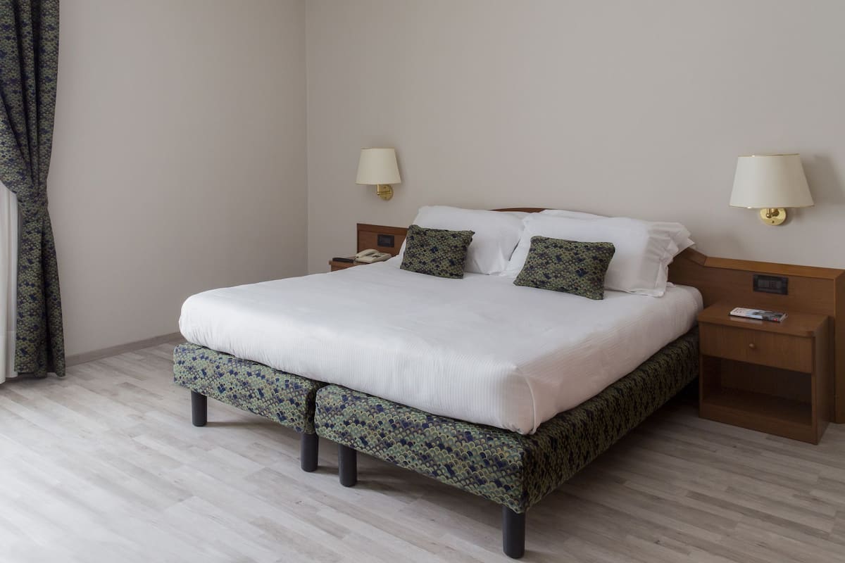 A neatly made bed with a patterned bedspread and pillows, two bedside lamps, and a wooden nightstand with a phone and a magazine.