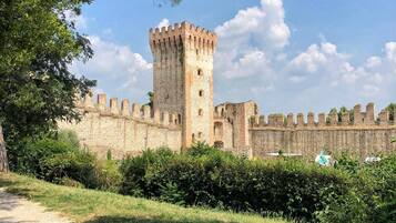 Eine historische Burg mit einem markanten Turm, umgeben von Grünflächen und einem Kiesweg.