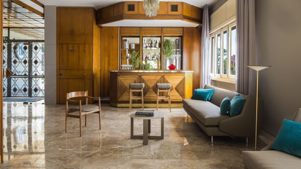 Una sala de estar moderna con zona de bar, paneles de madera, un sofá con cojines color turquesa y suelo de mármol.