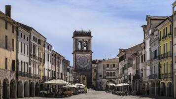 A cobblestone street with historic buildings on either side, a central clock tower, and outdoor seating areas.
