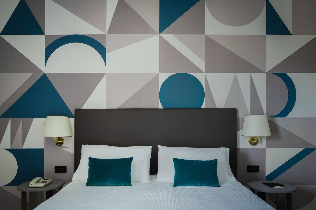 A hotel room with a large bed, two bedside tables, a nightstand, and a wall with geometric patterns.