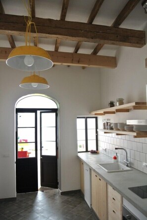 A kitchen with wooden beams, a white tiled backsplash, a sink, and a window with a view. - HoMe Hotel Menorca (Ciutadella de Menorca)