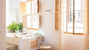 Une salle de bain avec une baignoire, un lavabo, un miroir et une fenêtre avec des rideaux.