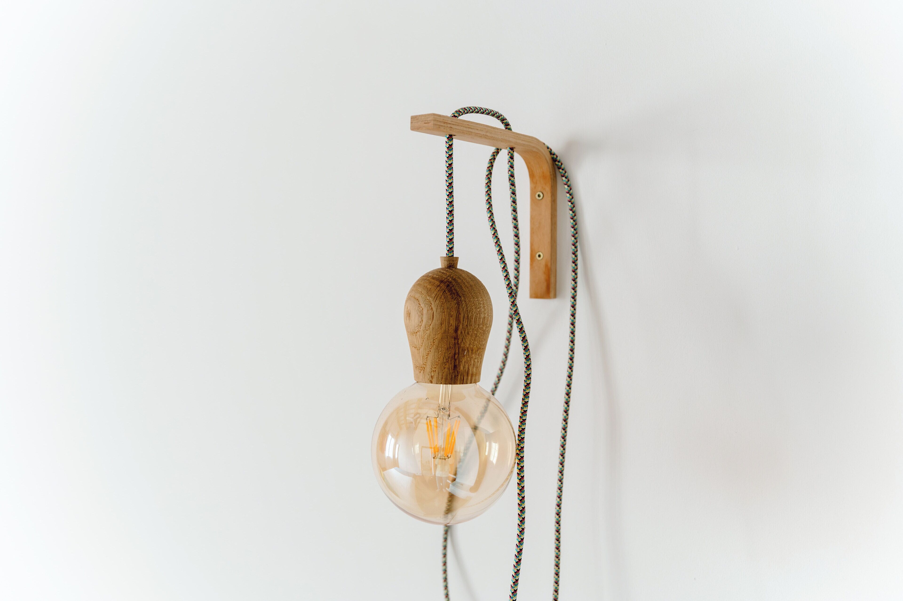 A wall-mounted light fixture with a wooden base and a clear glass bulb.