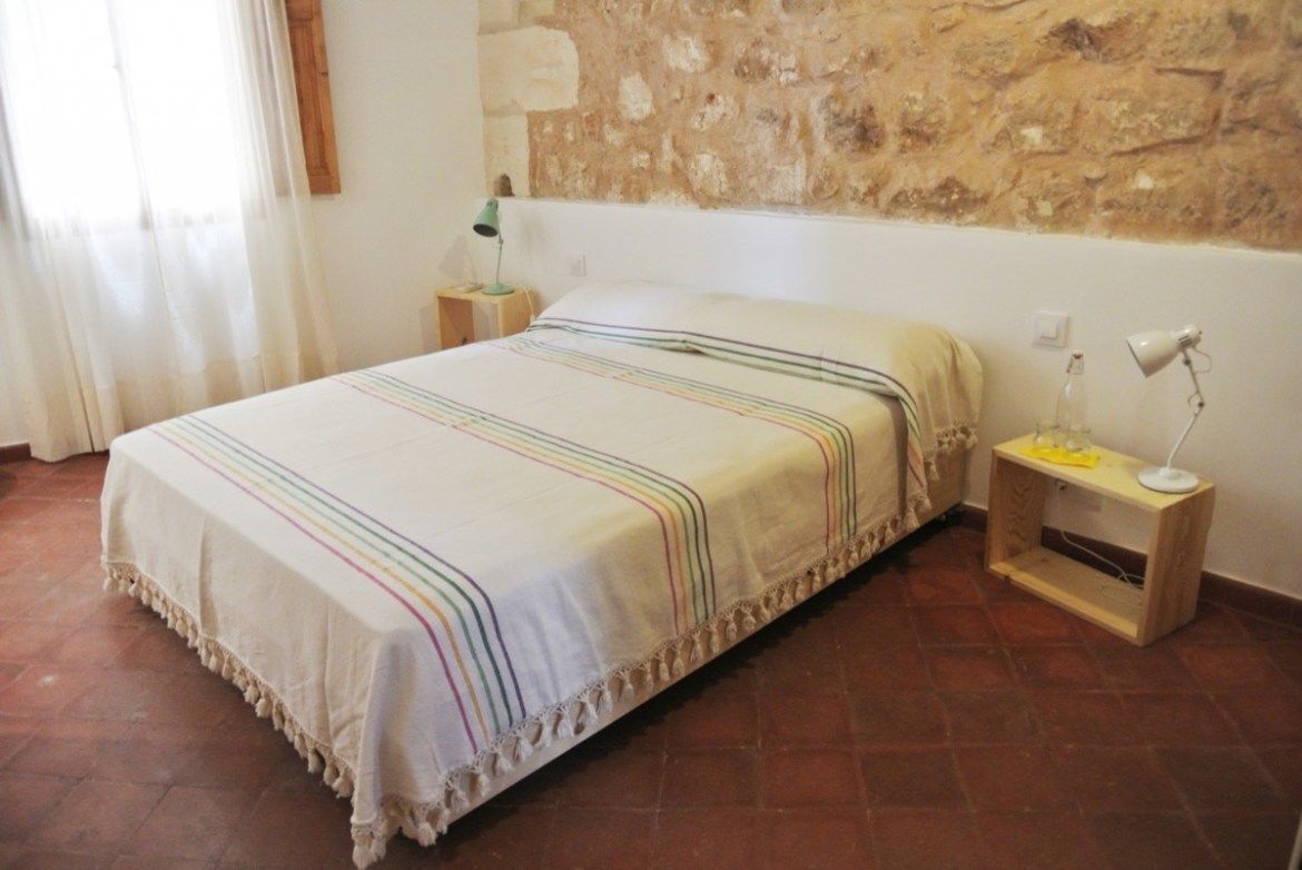 A bedroom with a bed, a nightstand, a lamp, and a stone wall.