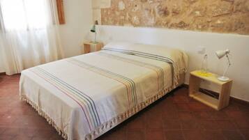A bedroom with a bed, a nightstand, a lamp, and a stone wall.