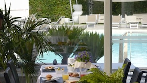 A dining table with breakfast items, a flower vase, and a view of a pool and lounge chairs. - La Villa Resort (Pieve a Nievole)