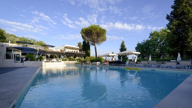 A swimming pool with lounge chairs and umbrellas, surrounded by buildings and trees. - La Villa Resort (Pieve a Nievole)