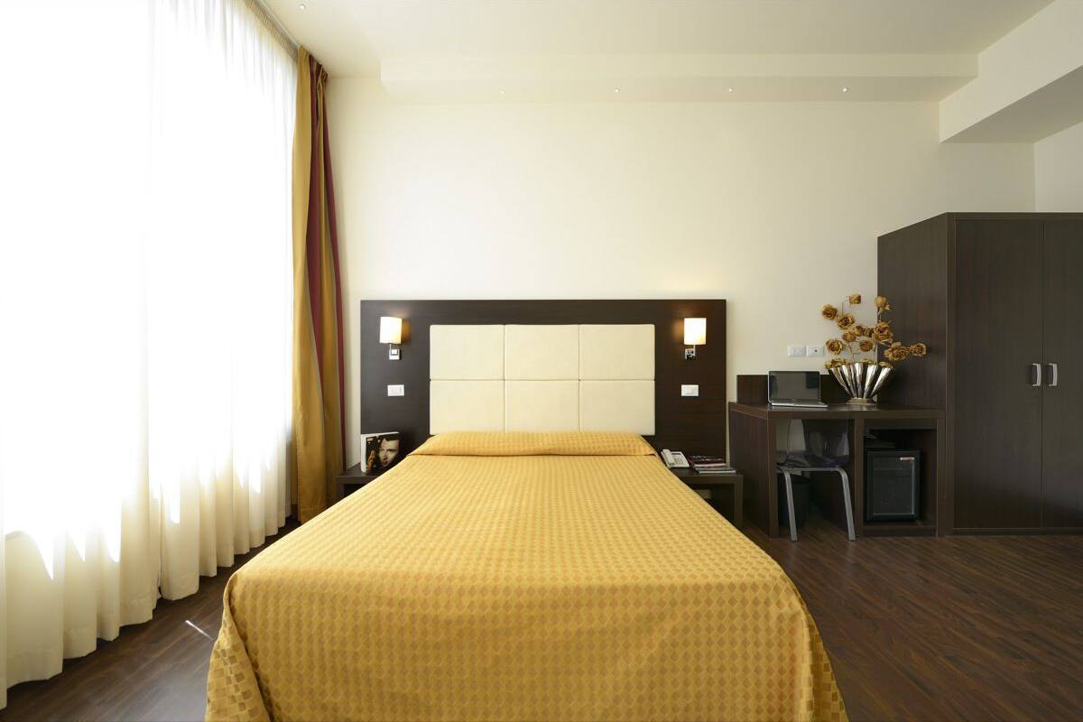 A hotel room with a large bed, a desk with a computer, and a wardrobe.