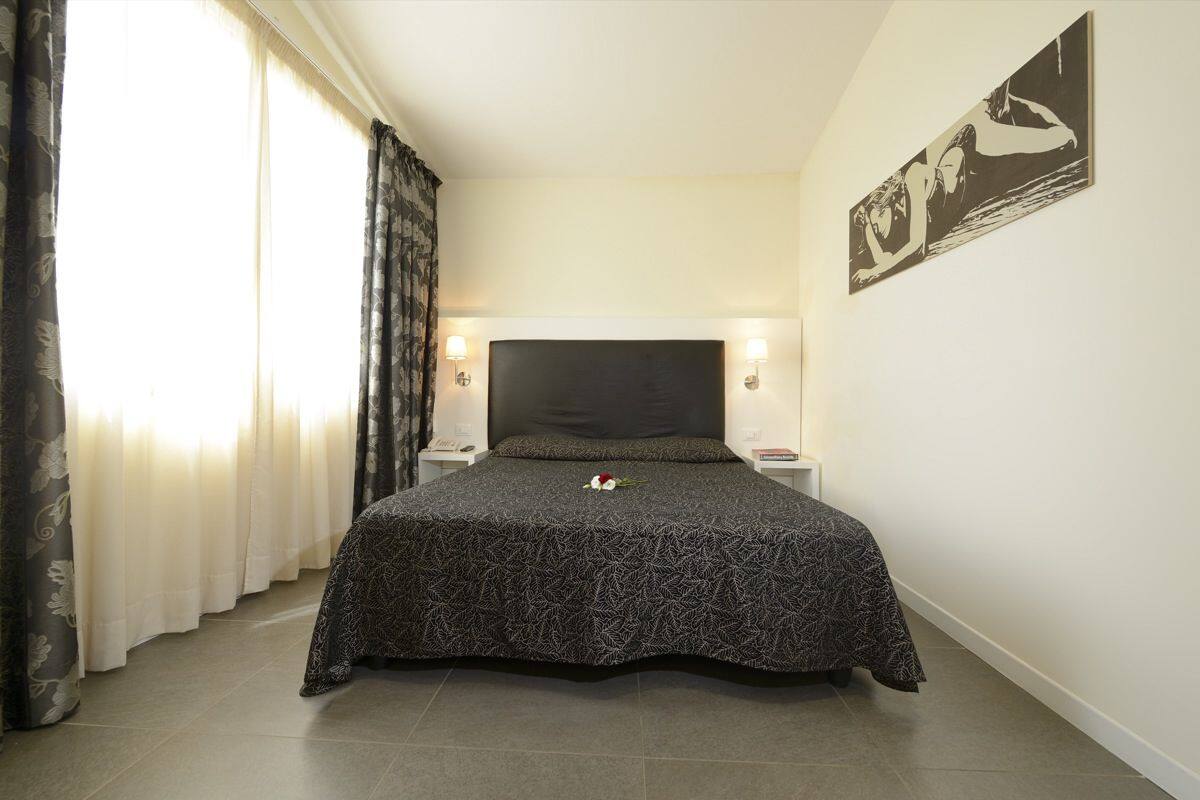 A bedroom with a large bed, a headboard, two bedside tables, and a wall-mounted artwork.