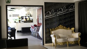 A reception area with a gold-trimmed white sofa, a wall with the resort's name and website, and a sign indicating the emergency exit. - La Villa Resort (Pieve a Nievole)
