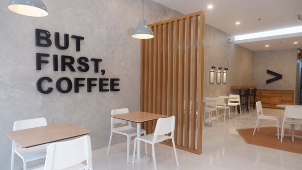 Un café moderno con un separador de madera, sillas y mesas blancas.