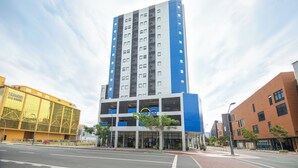 Un hotel de varios pisos con fachada azul y blanca, una entrada central y un letrero visible que dice 'Hop Inn'.