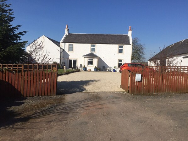A gated driveway leading to a two-story house with a gravel path.