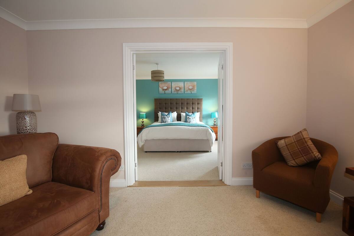 A bedroom with a bed, a brown sofa, and a brown armchair.