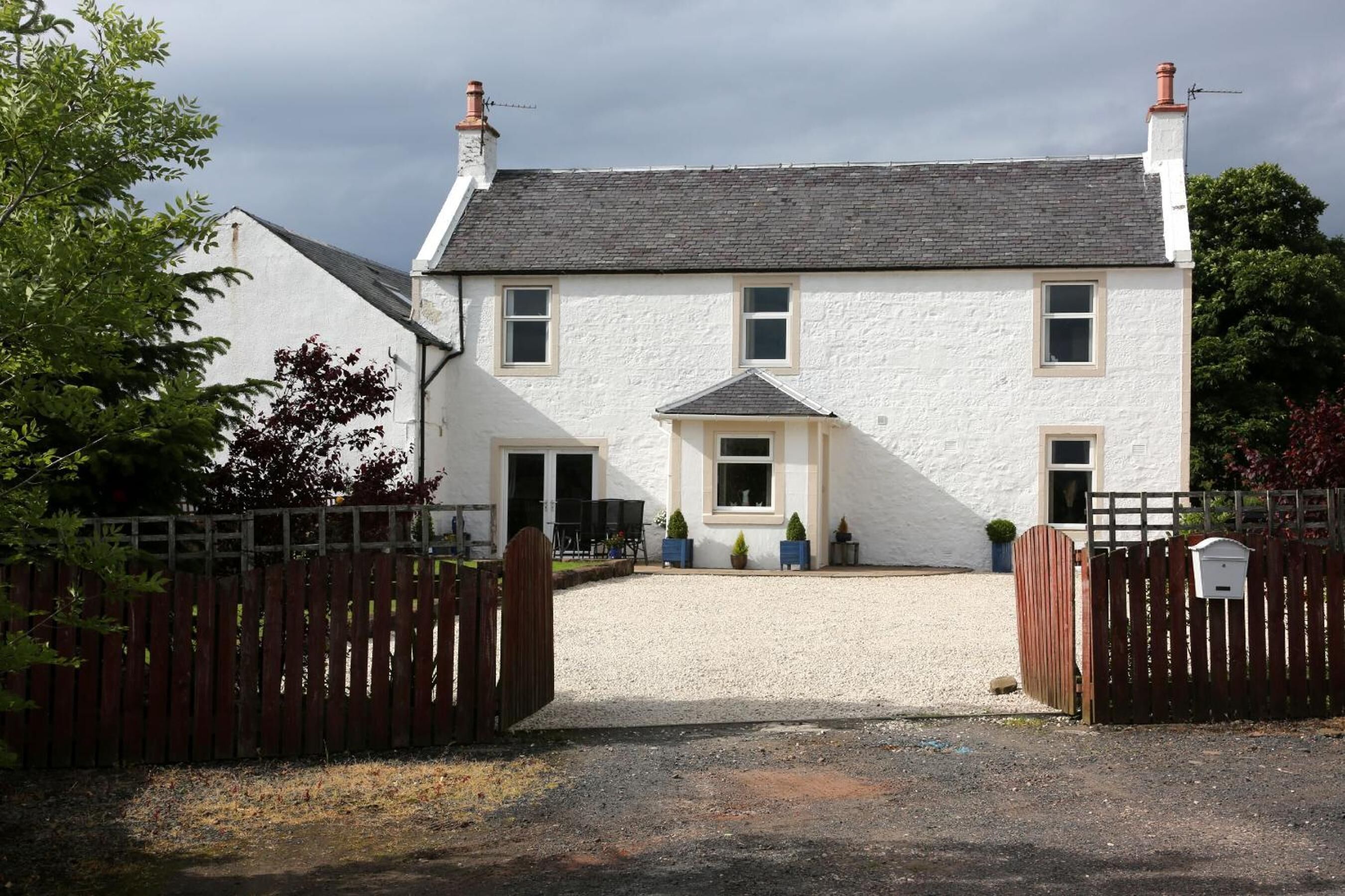 A two-story white building with a gravel driveway and a wooden gate.