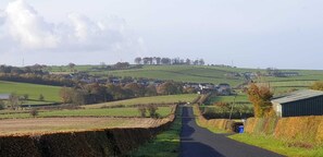 Une route de campagne bordée de champs et, au loin, de quelques bâtiments.