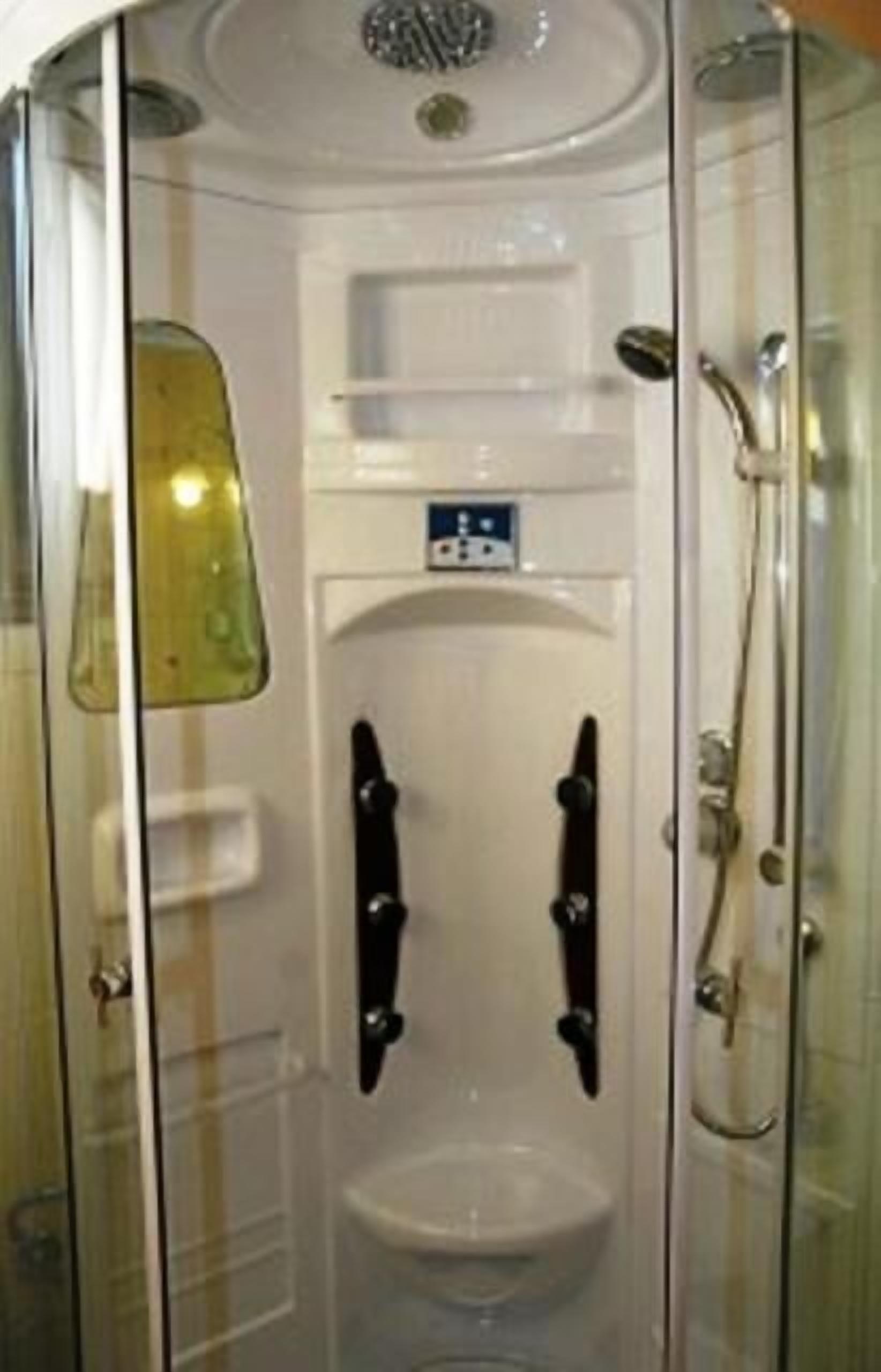 Een douchecabine met glazen wanden, een witte wastafel en een handdouche.