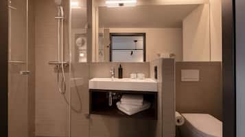 Un baño moderno con ducha de vidrio, un lavamanos blanco con espejo y un inodoro.