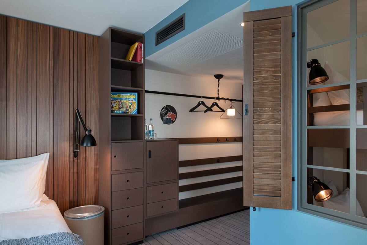 A bedroom with a bed, a wardrobe, a hanging light fixture, and a window with a view.