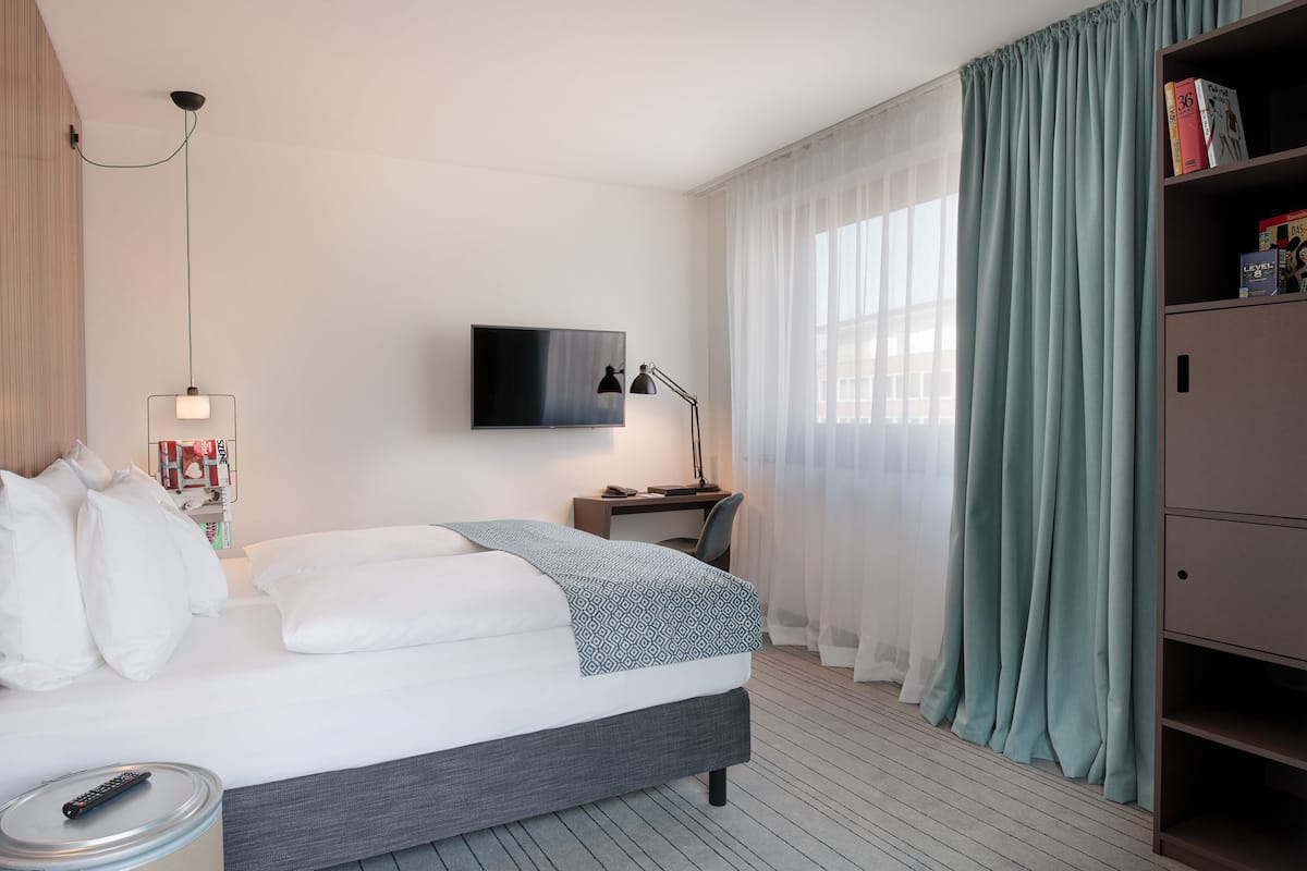 A hotel room with a bed, a desk, a TV, and a bookshelf.