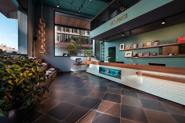 A modern reception area with a wooden reception desk, a large aquarium, and a view of the cityscape through large windows. - Pierdrei Hotel HafenCity Hamburg (Hamburg)