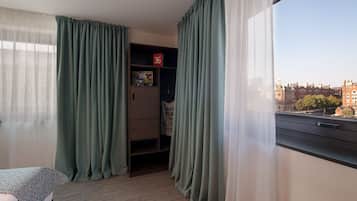 Una habitación con cama, armario y ventana con vista a edificios.