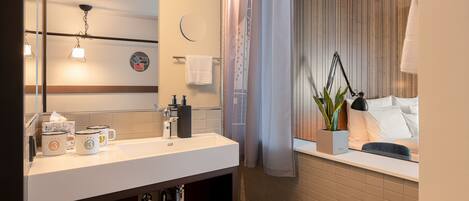 A modern bathroom with a white sink, mirror, and towel rack. There is a plant on the windowsill and a towel folded on the counter.
