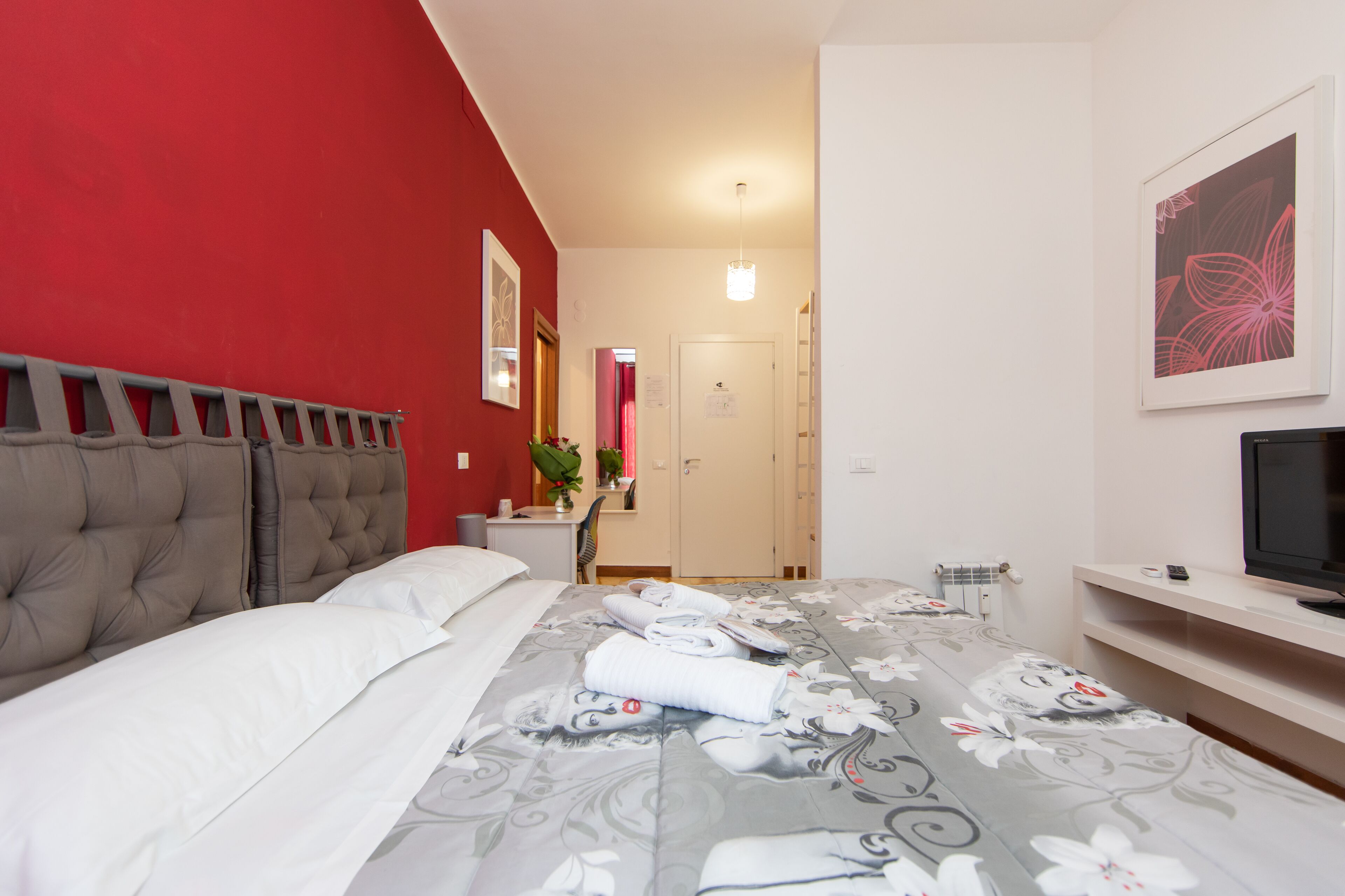 A hotel room with a bed, a TV, a desk, and a bathroom visible in the background.