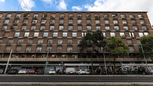 A multi-story brick building with numerous balconies, a row of parked cars, and a clear sky. - Imperiale Roma Trastevere (Rome)