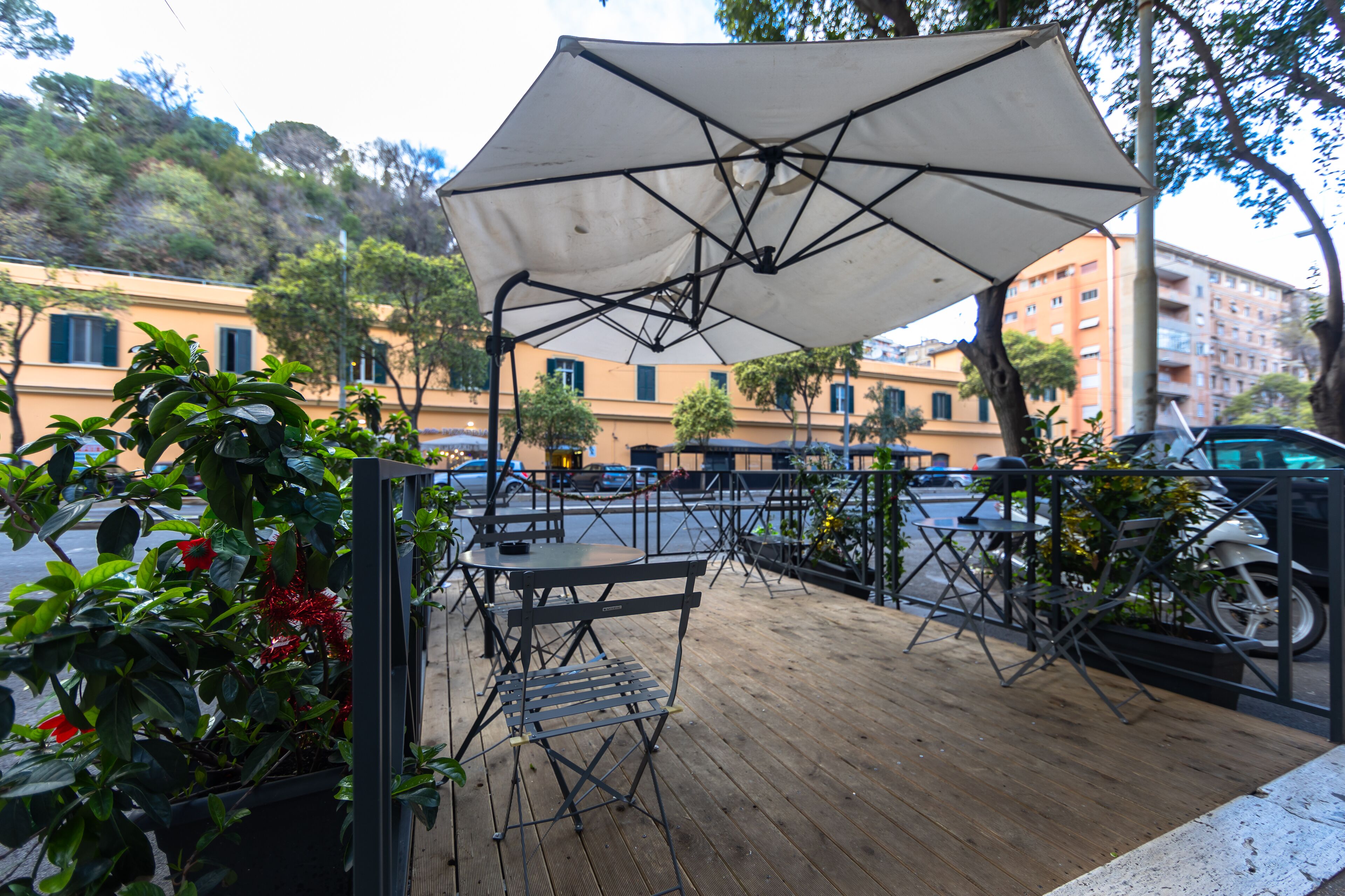 An outdoor patio with tables and chairs, a large umbrella, and potted plants.