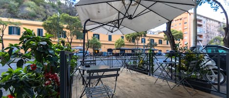 An outdoor patio with tables and chairs, a large umbrella, and potted plants.