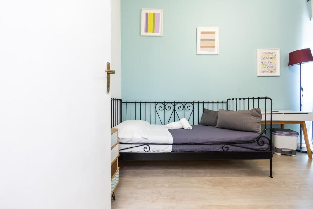 A single bed with a metal frame, a bedside table, a lamp, and a wall with three framed pictures.