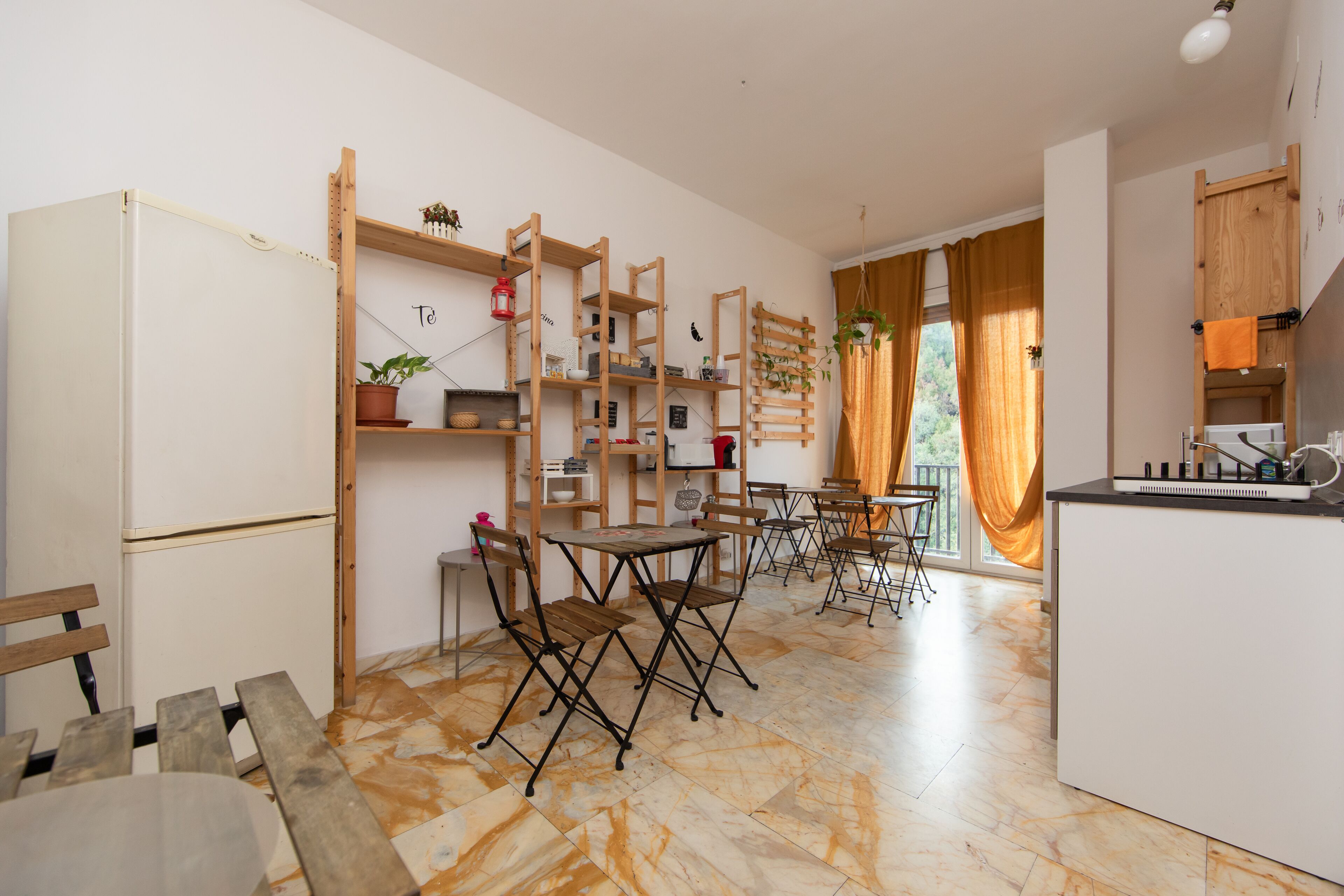 Une cuisine avec des étagères en bois, un réfrigérateur blanc et un coin repas doté de chaises et de tables pliantes.
