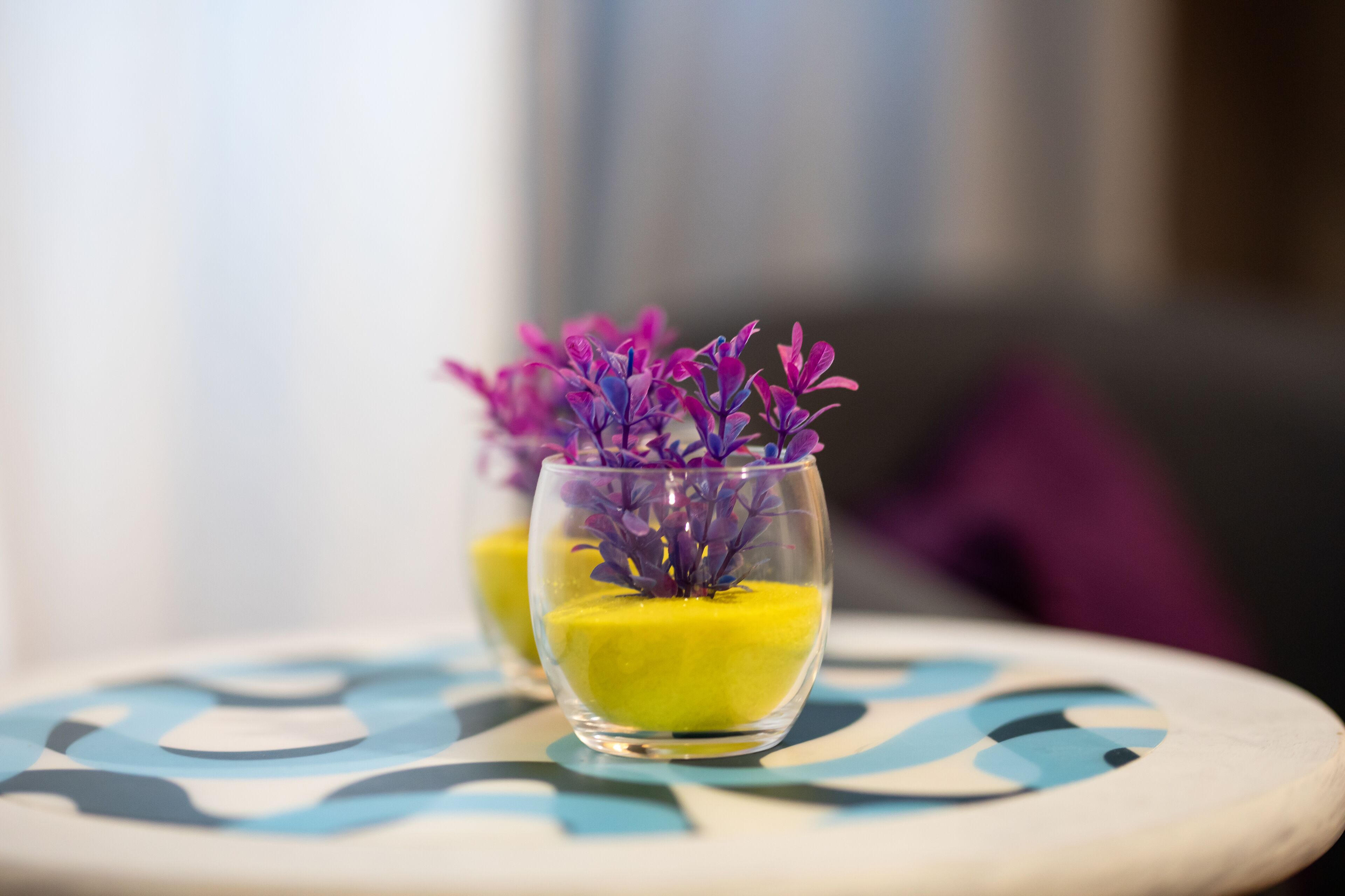 Deux verres de dessert jaune, décorés de fleurs violettes, sont posés sur une table à motifs bleus et blancs.