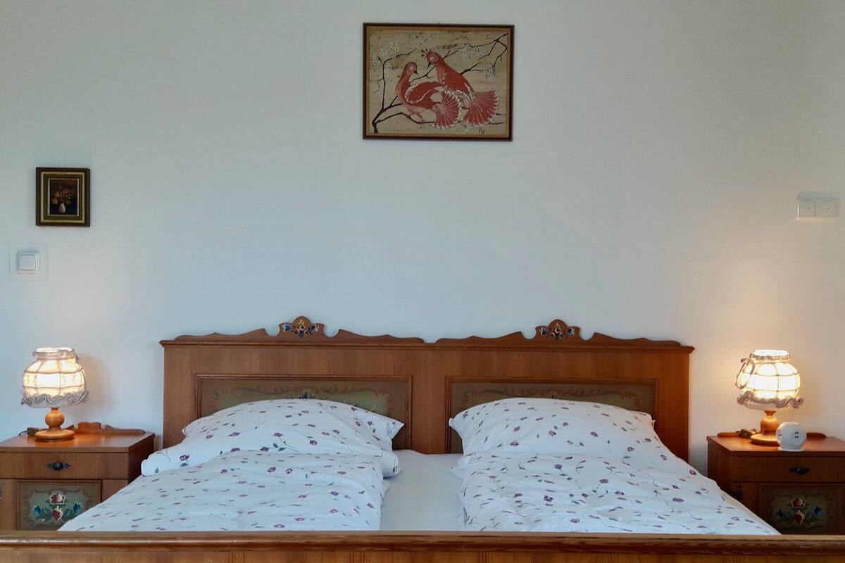 A double bed with floral bedding, wooden headboard, bedside tables with lamps, and a framed artwork on the wall.