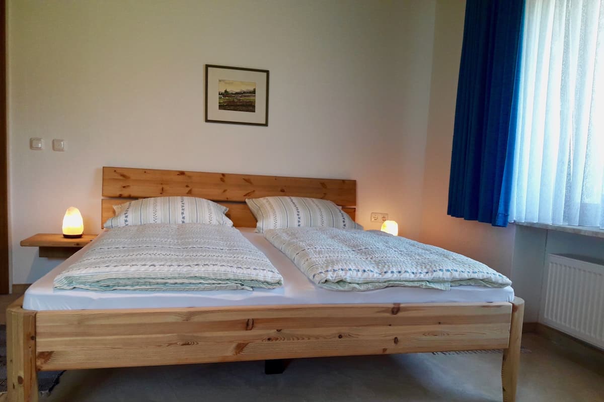 A double bed with a wooden frame, two bedside tables with lamps, a framed picture on the wall, and a window with curtains.