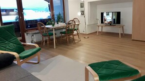 Un salon moderne comprenant un coin repas, un téléviseur et offrant une vue sur un paysage enneigé grâce à de grandes fenêtres.